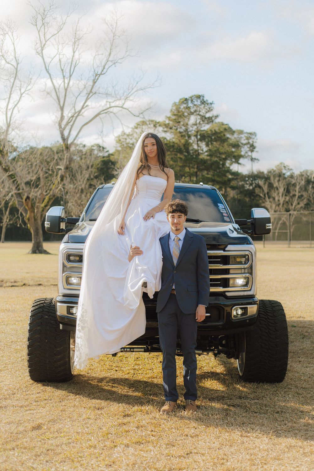 Wedding photos featuring a lifted black pickup truck as a rustic backdrop in a grassy field.