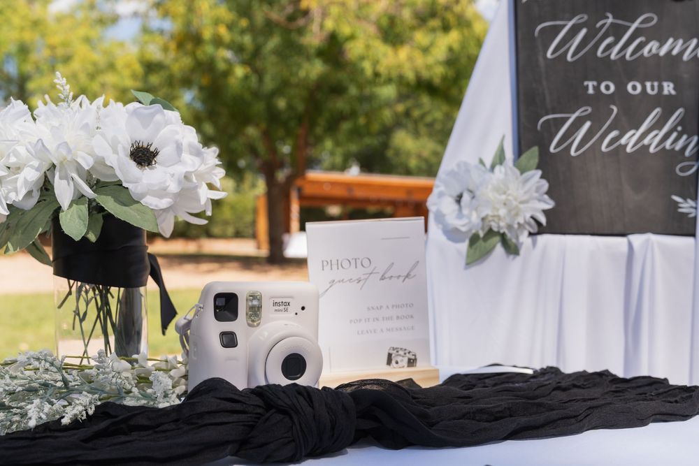 Wedding decor details including welcome signs, white flowers, and instant cameras arranged on tables at an outdoor venue.