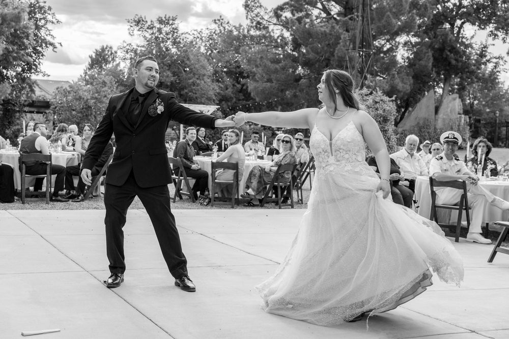 Black and white photo of bride and groom sharing first dance at outdoor wedding reception with guests seated in background.