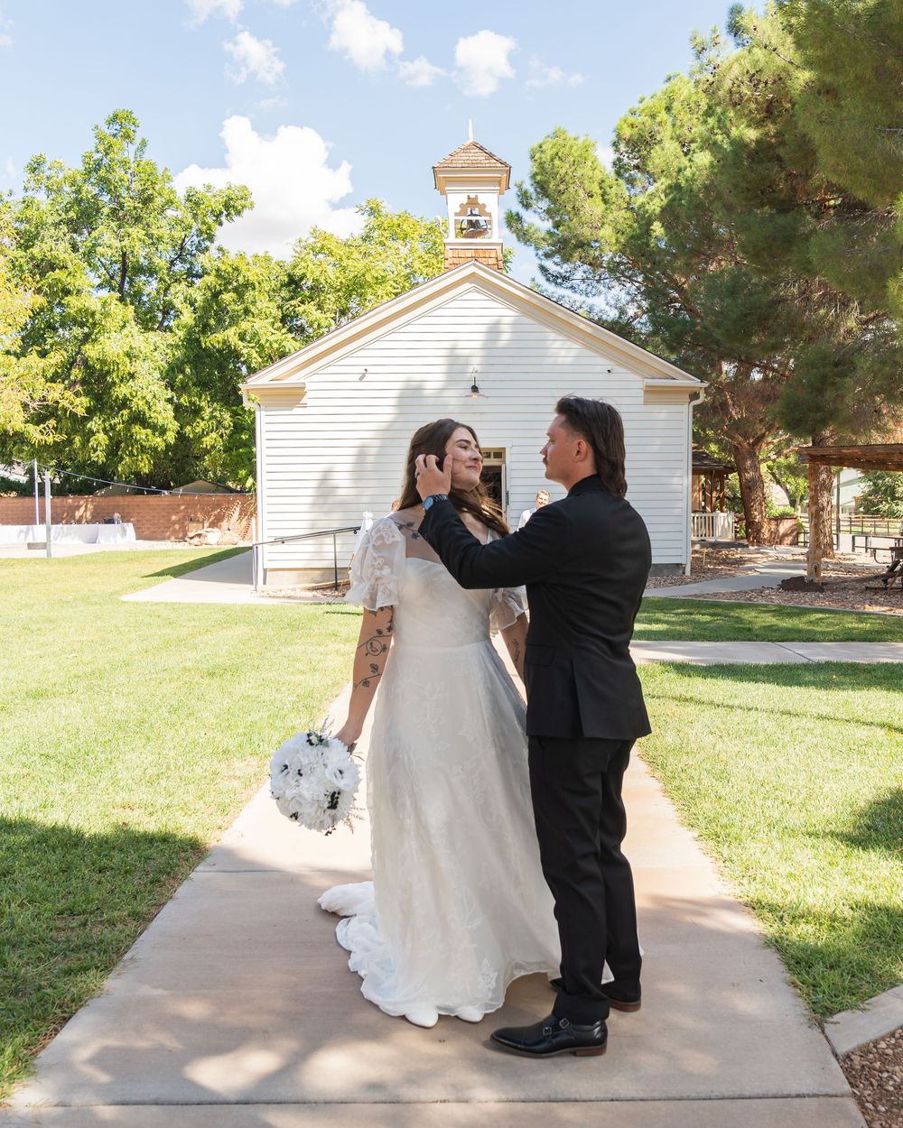 A couple shares a romantic moment outside a charming white chapel in Virgin, Utah for their wedding day.