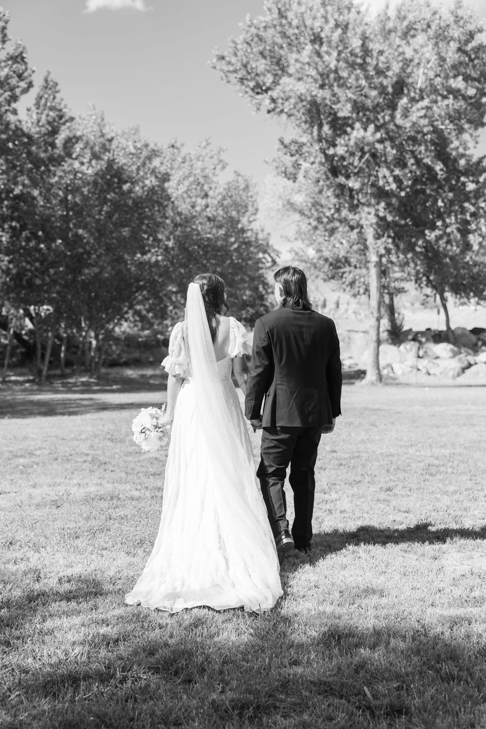Black and white wedding photo series showing couple walking away through grassy field in traditional formal attire.