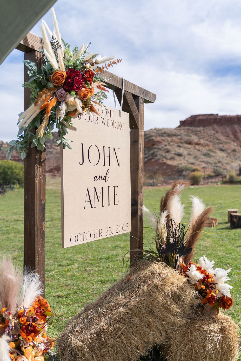 Rustic wedding signage decorated with autumn florals and hay bales against a desert mountain backdrop.