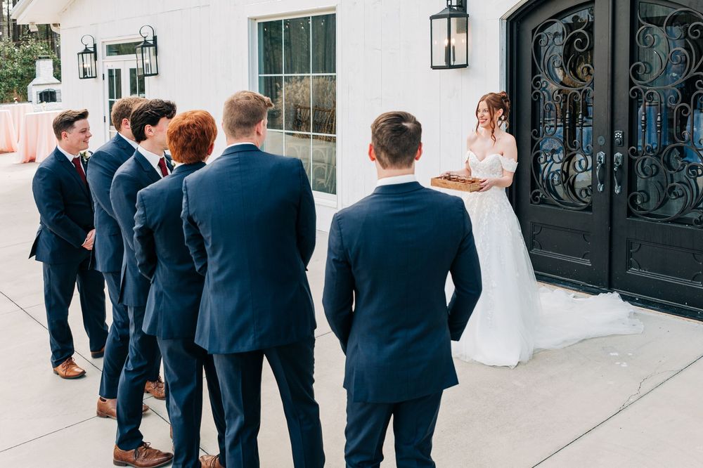Wedding party members in navy blue suits stand together outside a white building entrance.