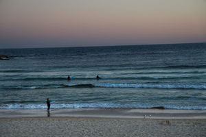 Bondi Beach with waves rolling in and the sun setting painting the sky shades of yellow and orange