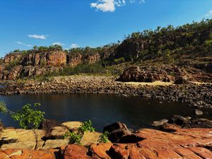 A beautiful body of water with orange coloured rocks and areas of greenery in the Northern Territory