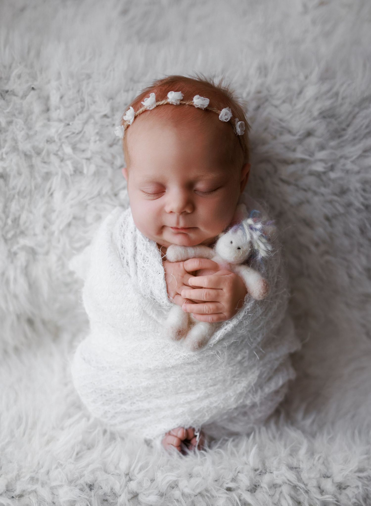 Photograph of a newborn baby girl swaddled in white with a unicorn stuffy