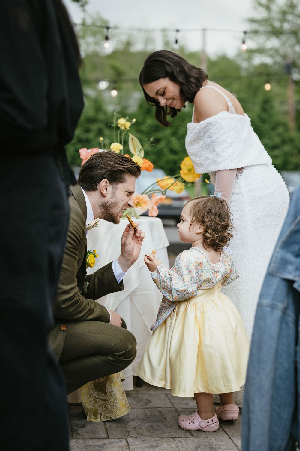 A tender moment at a wedding as a man in a brown suit kneels down to interact with a small child in a yellow dress.