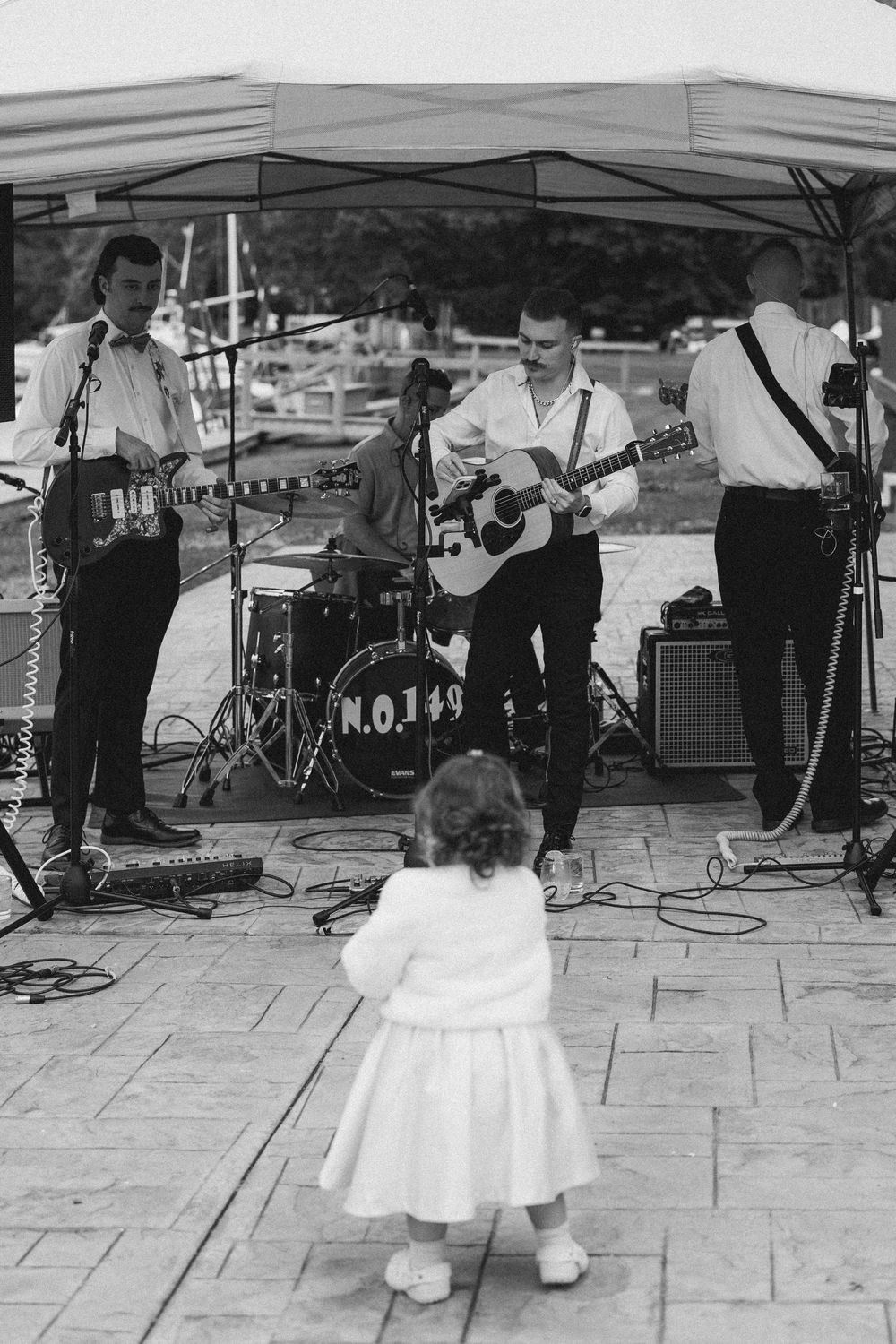 A sequence of black and white photos showing a small child in a white dress dancing at an outdoor music performance.