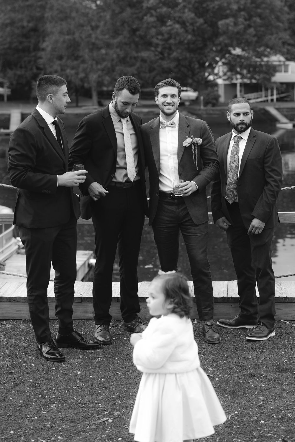 A series of black and white wedding photos showing groomsmen in suits and a small flower girl in a white dress.