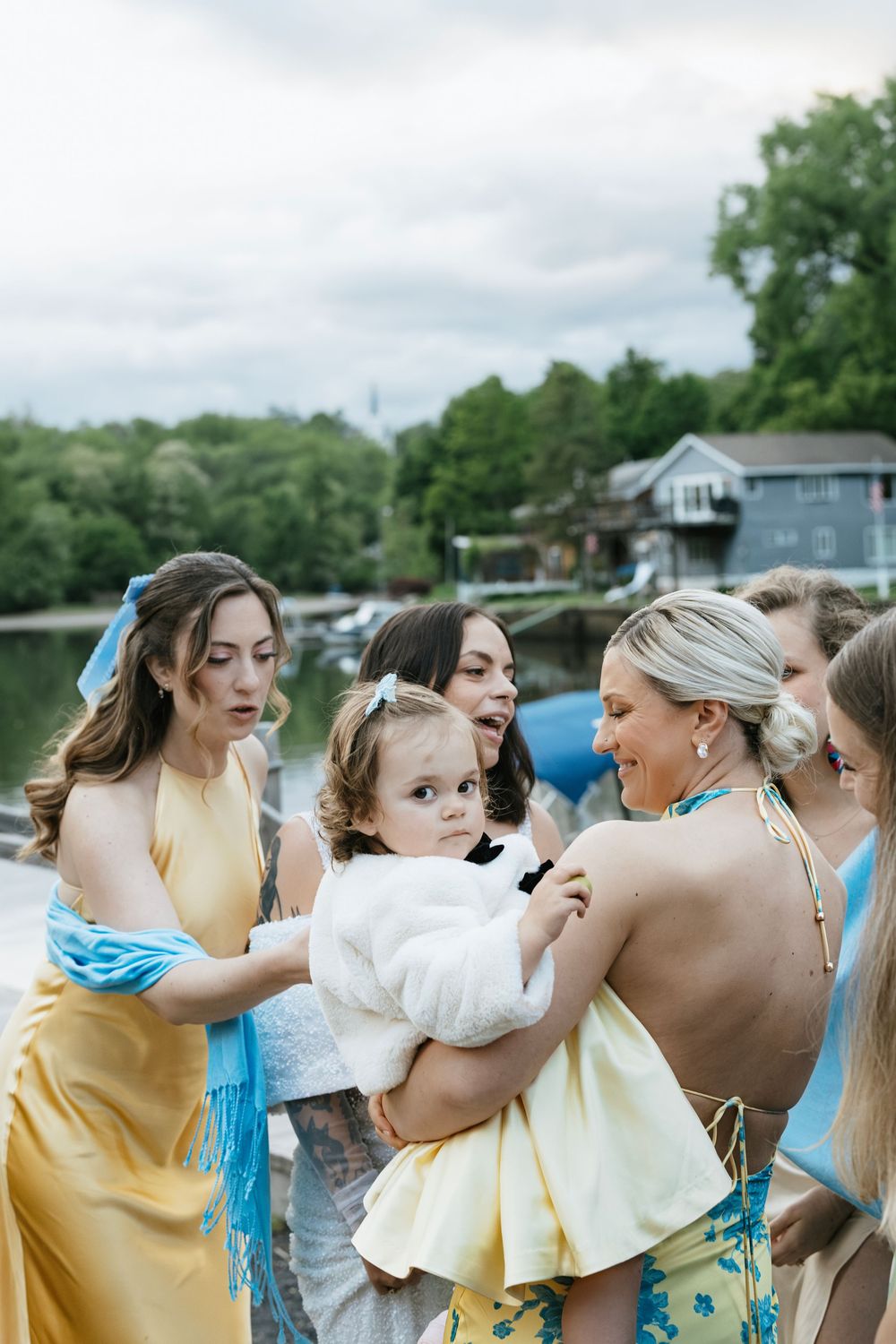 A group of bridesmaids in yellow dresses share playful moments and laughter during an outdoor wedding celebration.
