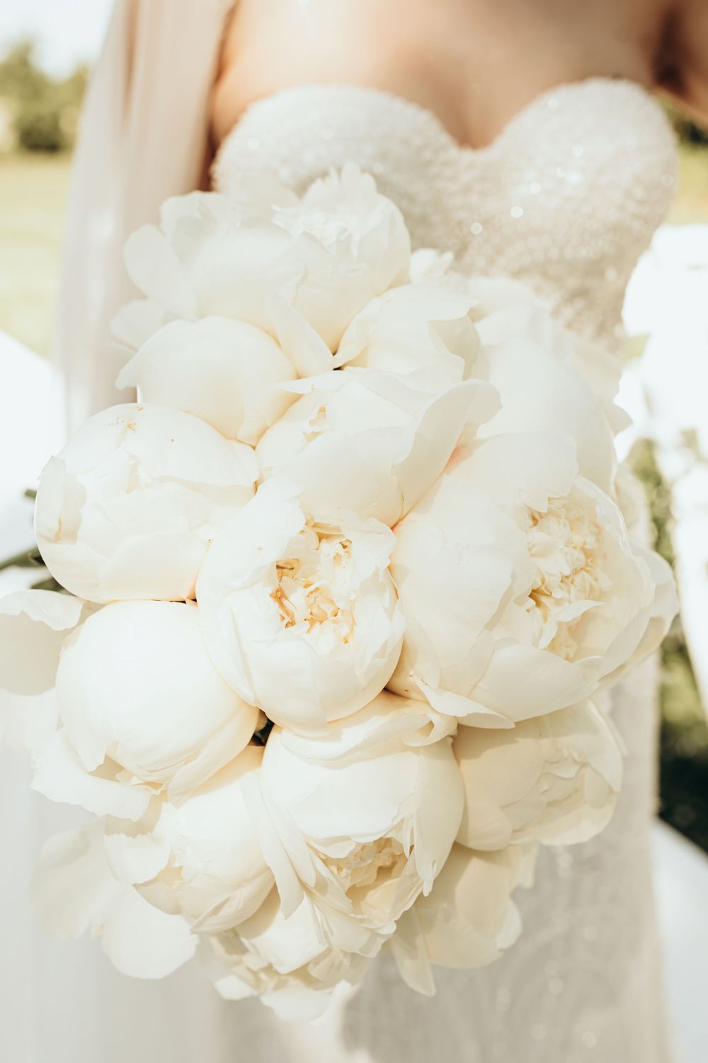Close-up of an elegant white peony bridal bouquet against a wedding dress background.