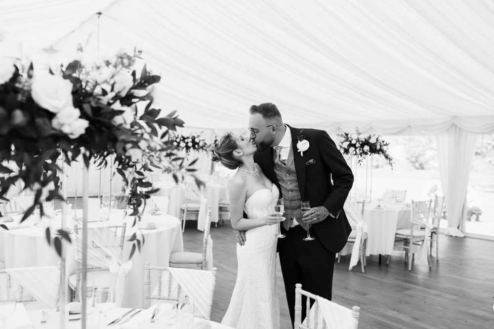 Wedding reception setup under a white tent with elegant table settings and floral centerpieces.