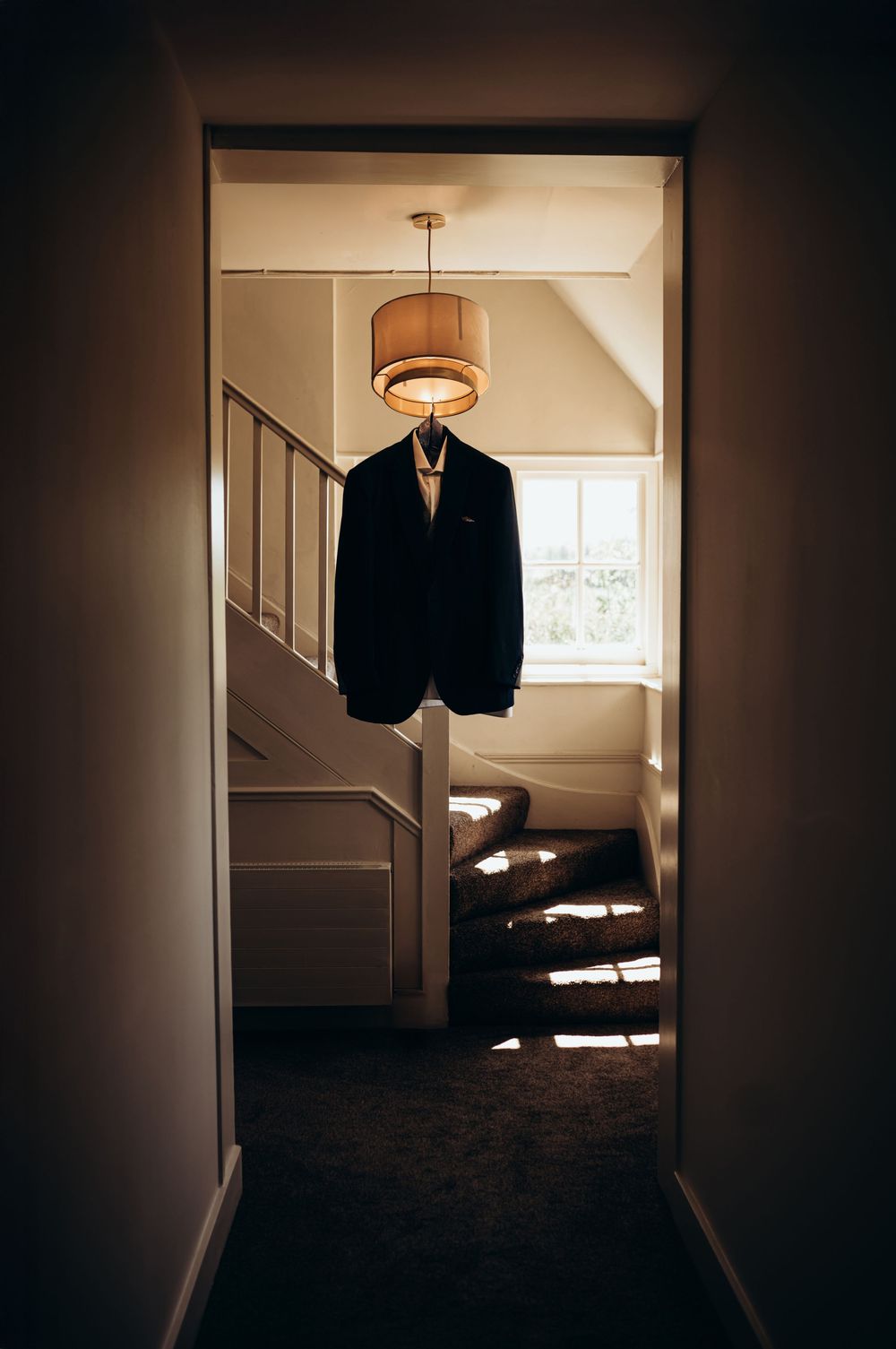 A dark silhouette of a suit jacket hangs in a dimly lit hallway with stairs and ambient lighting.