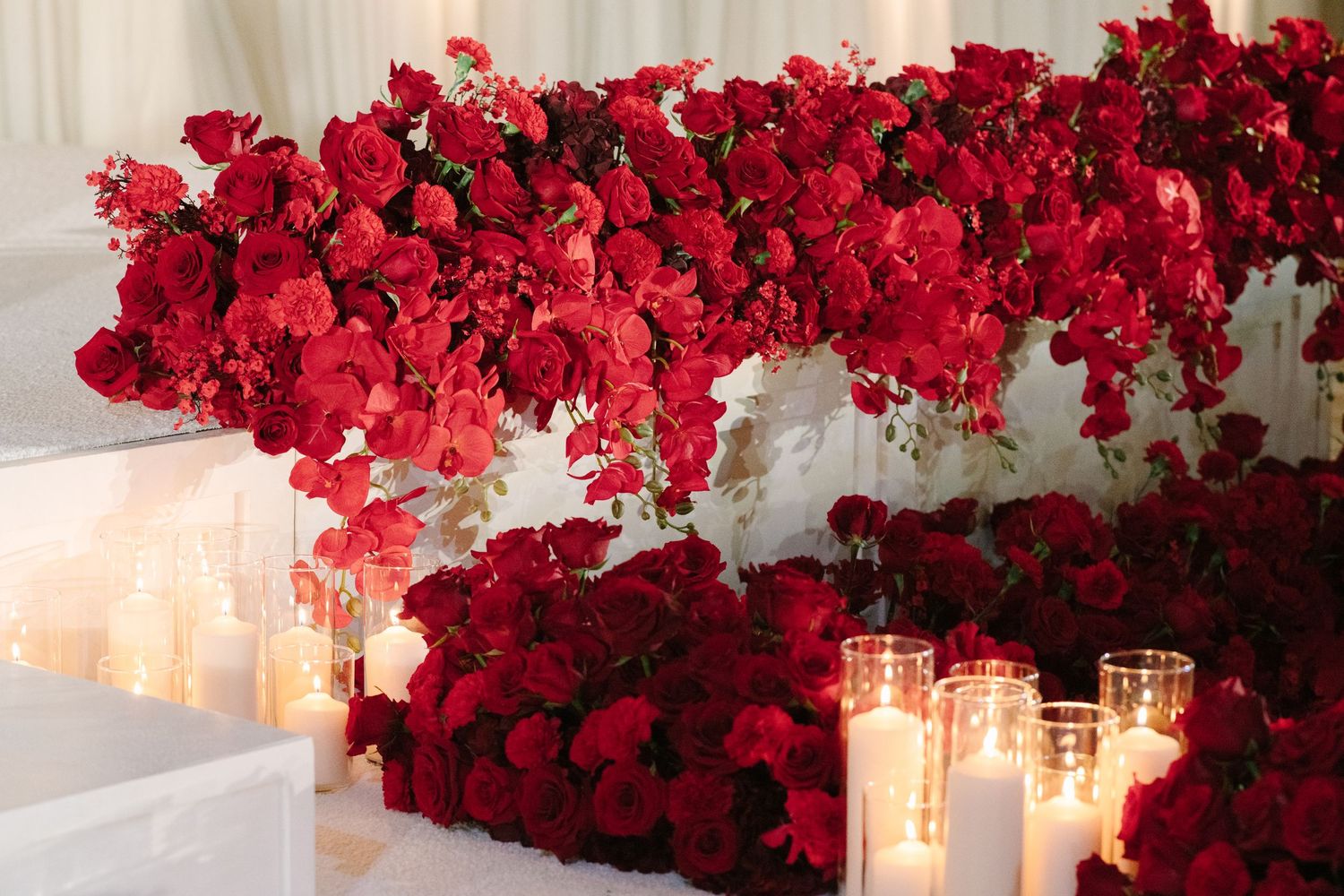 Elegant wedding aisle lined with lush red roses, white candles, and draped fabric creating a romantic ceremonial setting.