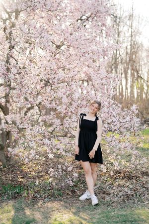 Artistic portrait series amid blooming cherry blossom trees showcasing black dress and white sneakers.