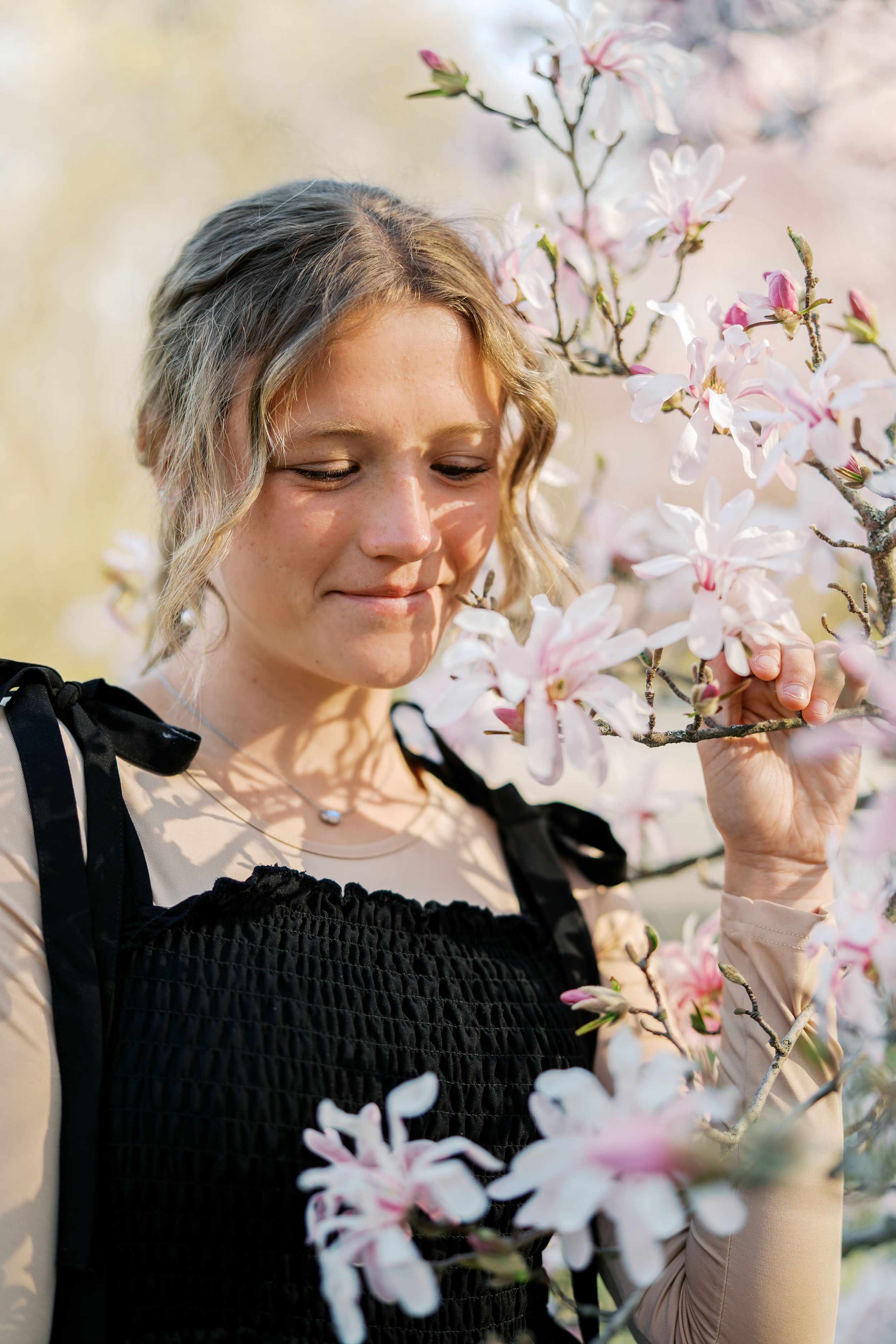 A dreamy spring portrait among blooming magnolia flowers with soft natural lighting and a black top.