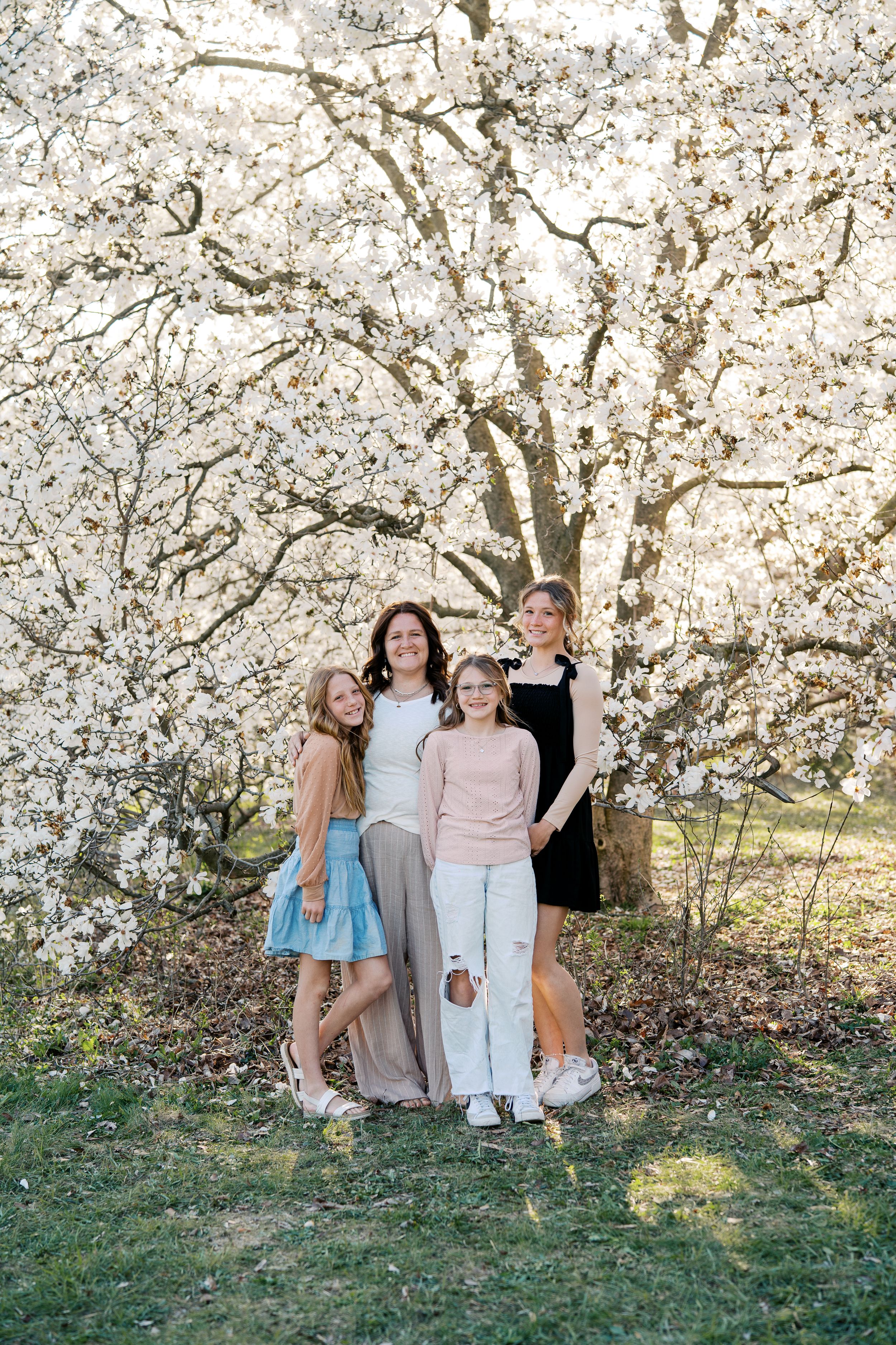 Children sitting together under blooming cherry blossom trees in spring garden setting.