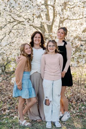 A group poses together outdoors against a backdrop of blooming spring trees in coordinated neutral-toned outfits.