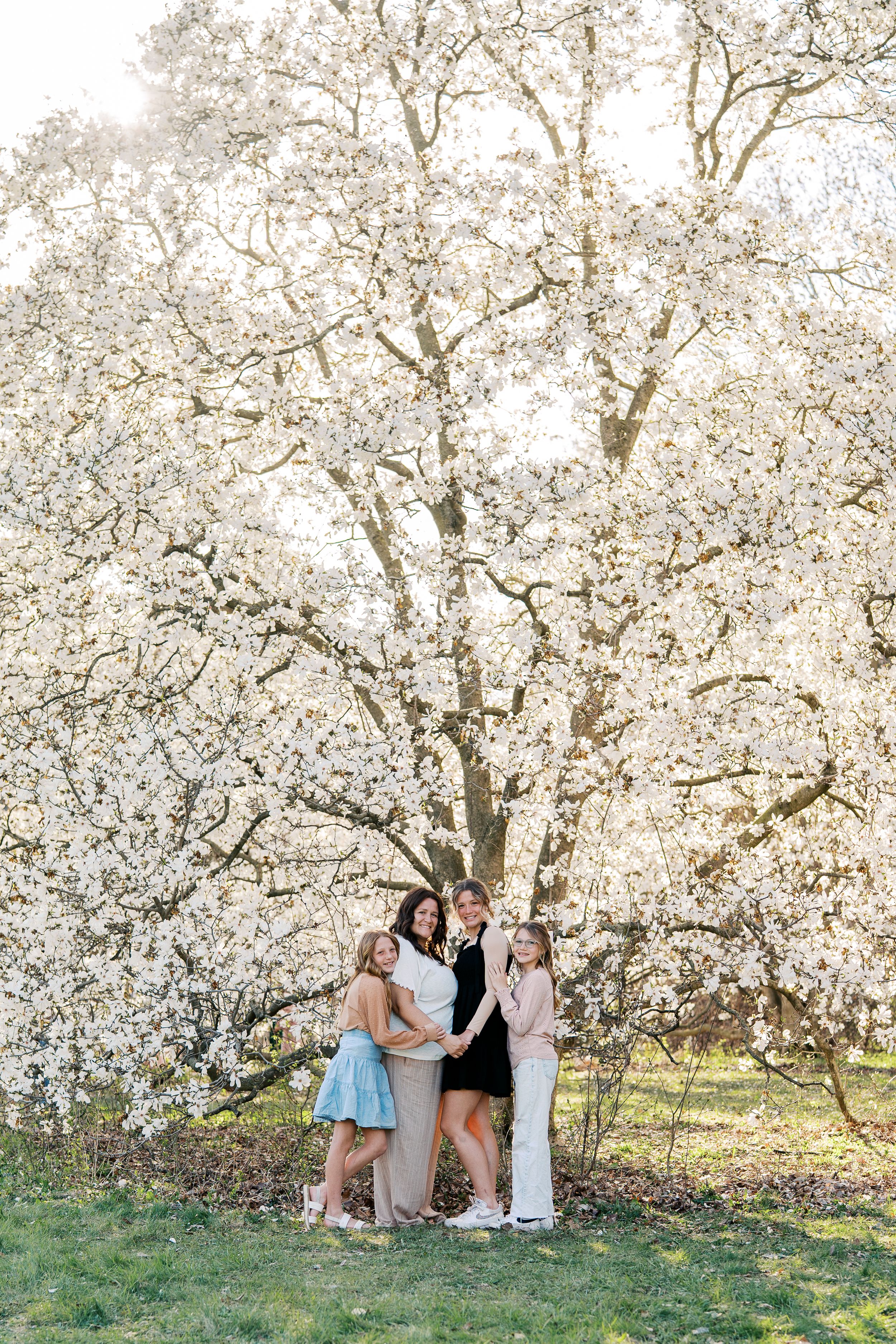 A group gathers under blooming white cherry blossom trees in a spring photo session.