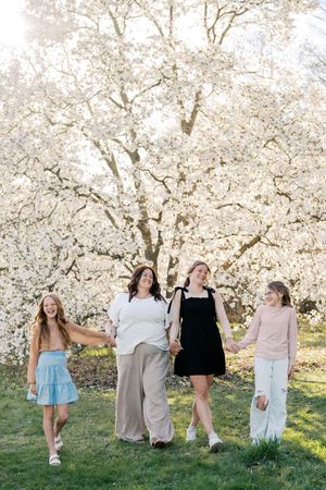 Friends gathered beneath flowering trees in a park wearing casual spring outfits.