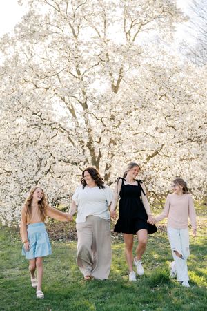 Friends walking and laughing together under flowering cherry blossom trees on grassy hill.