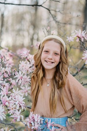 Spring portrait series with delicate pink magnolia blossoms framing joyful expressions in a natural outdoor setting.