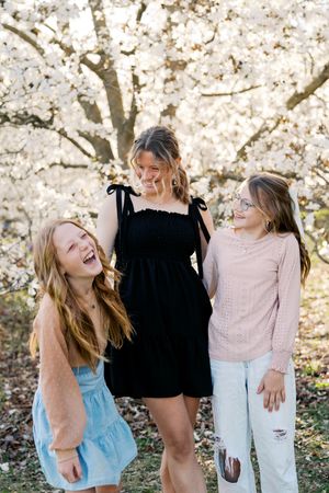 A series of candid photos showing joyful laughter and interaction among friends against a backdrop of spring blossoms.
