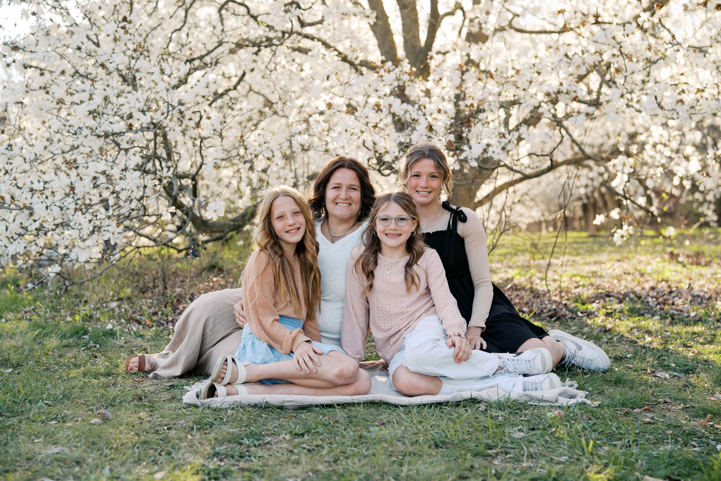 Family group lounging on grass under blooming spring cherry trees during outdoor photo session.