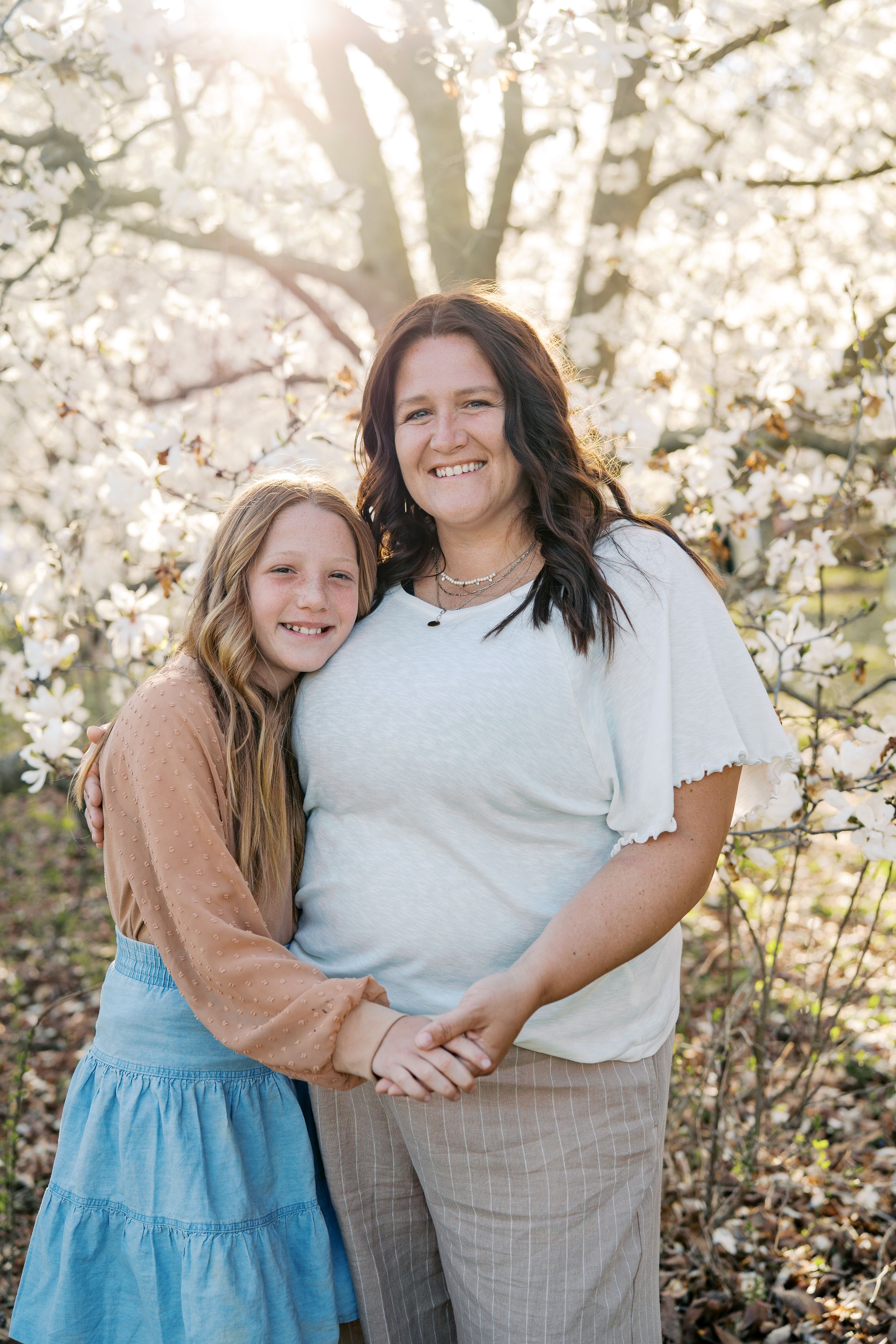 Candid portrait of friends embracing and laughing under blooming spring trees.