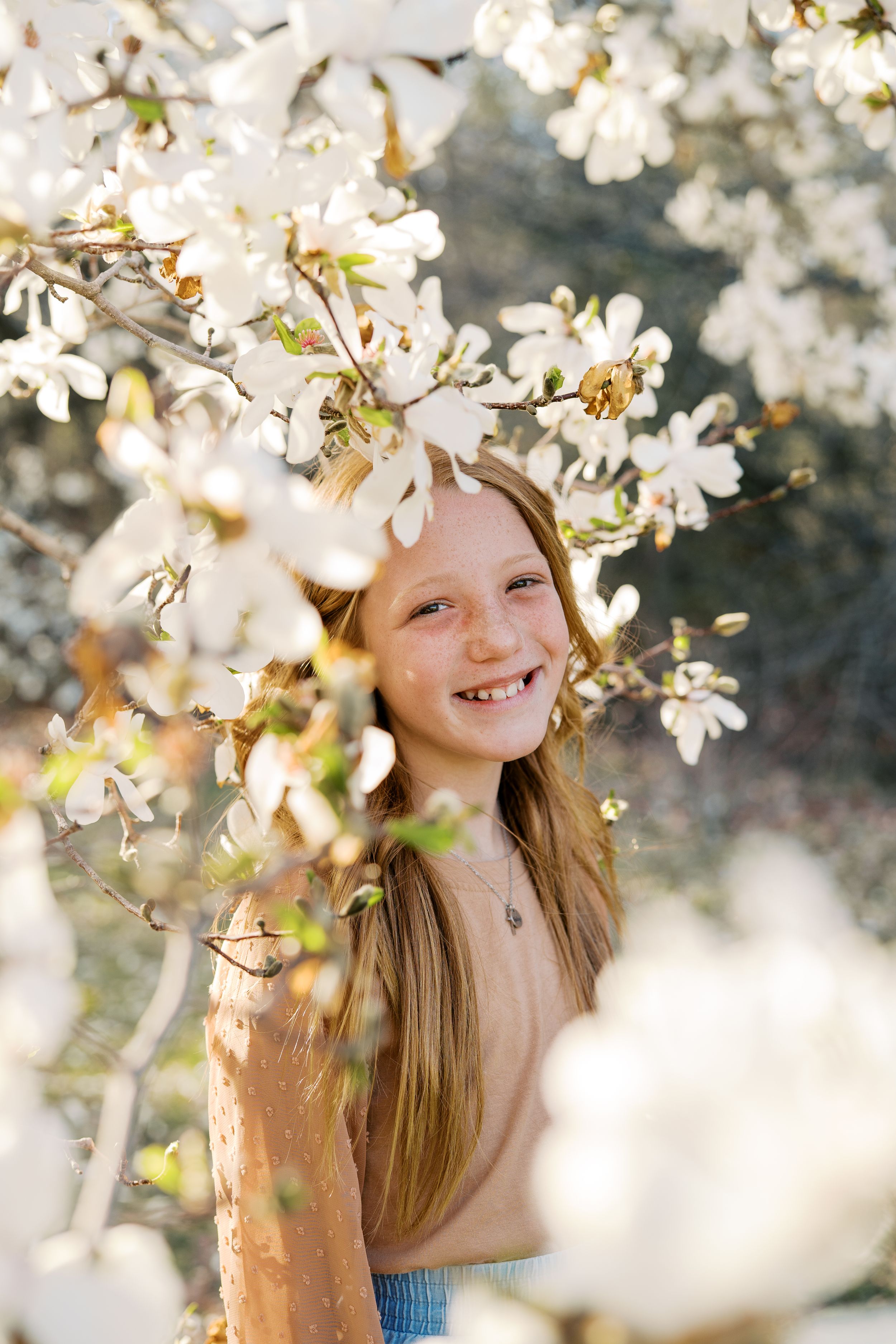 Candid springtime portrait among blooming white cherry blossom branches in soft sunlight.
