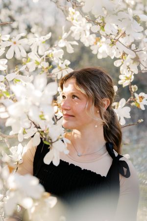 Close-up portrait among white magnolia blossoms in soft spring light.