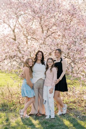 People enjoying a spring photoshoot under pink cherry blossoms with sunlight filtering through.