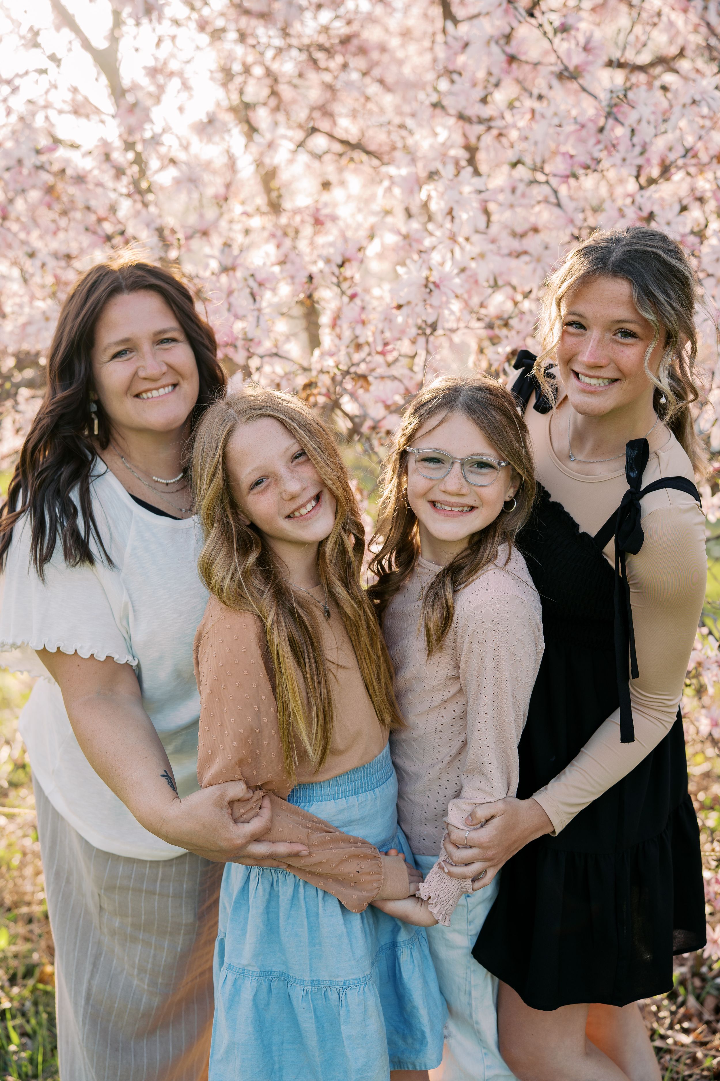 Friends sharing laughter and embraces under pink cherry blossom trees in spring.