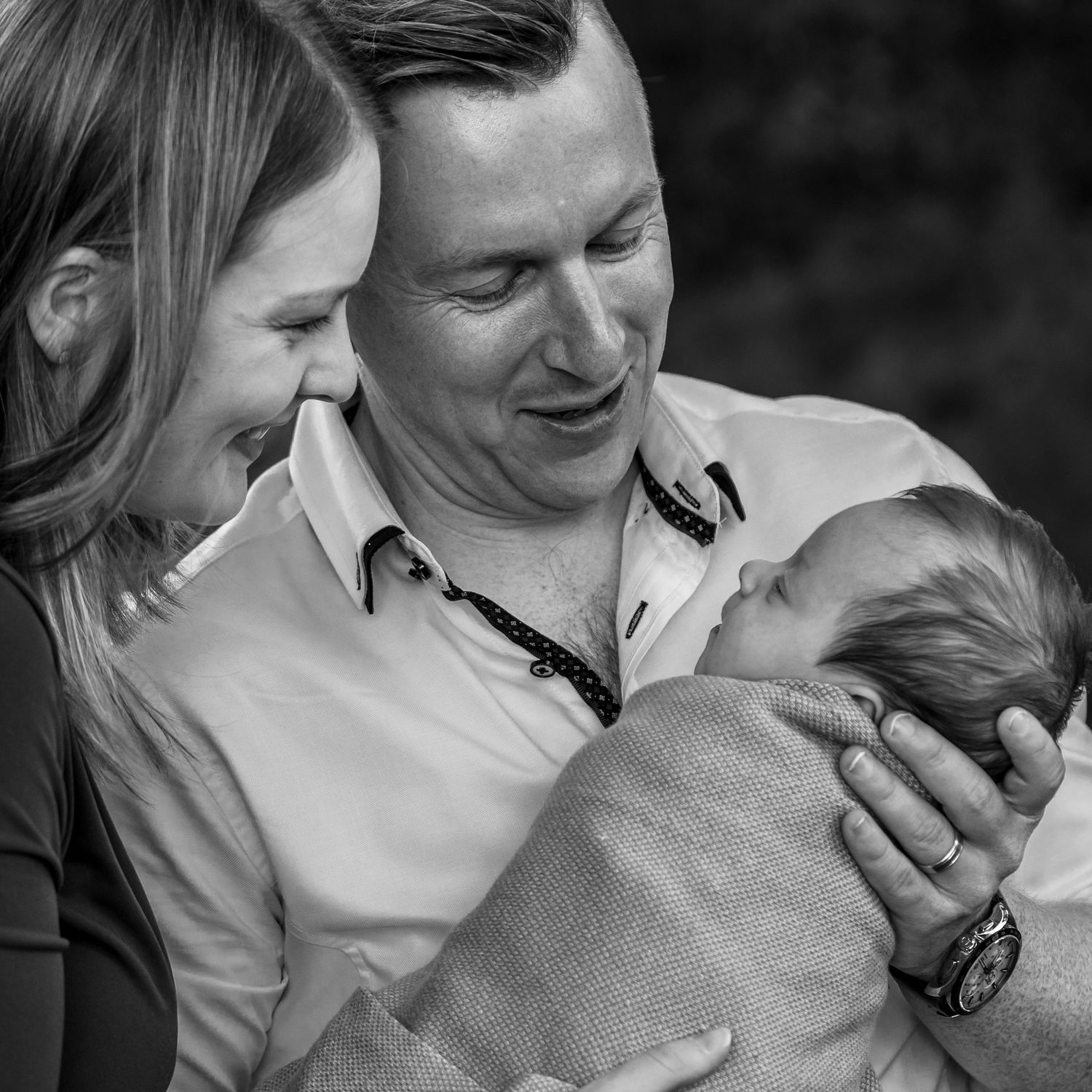 Natural, unposed black and white newborn photo with parents holding their baby in soft light