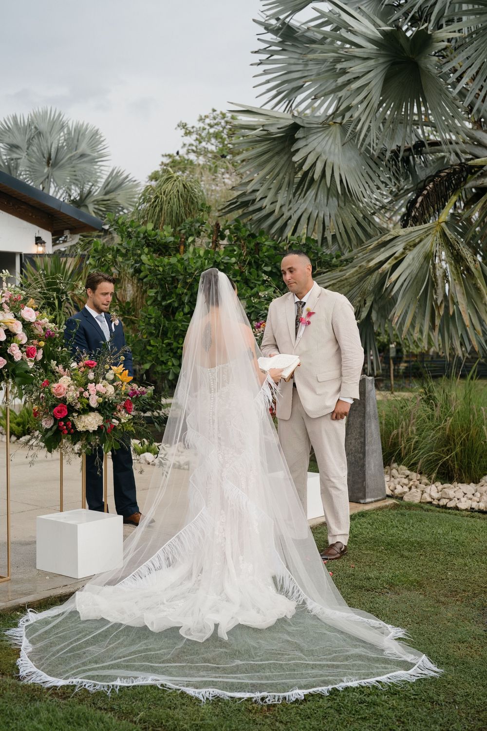 A wedding ceremony setup in a lush garden with palm trees and floral arrangements creating a romantic tropical atmosphere.