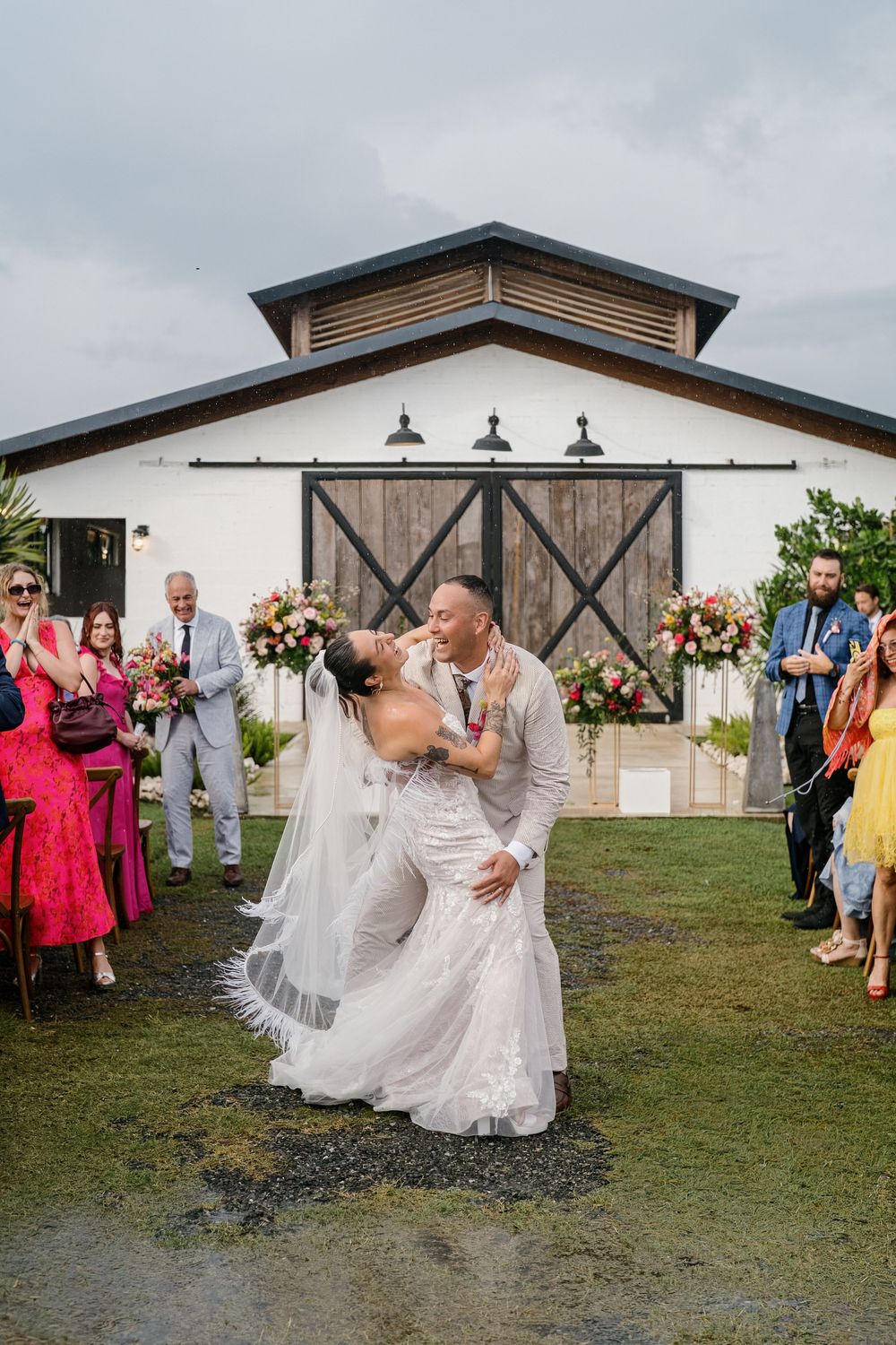 A romantic wedding celebration outside a rustic barn venue with wooden doors and floral arrangements.