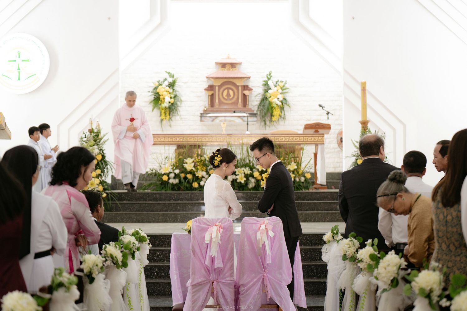 Bride and groom kneeling at church altar during a traditional Catholic wedding ceremony.