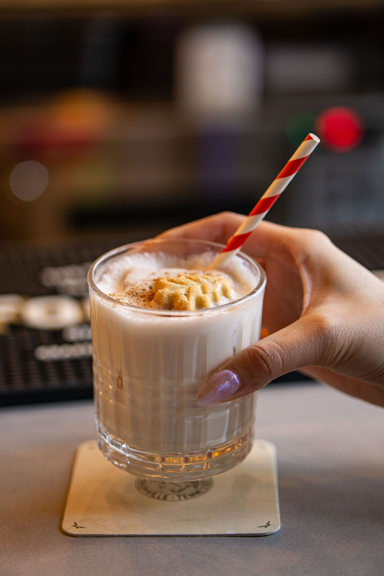 A sequence of hands holding glass cups filled with creamy coffee drinks and decorative straws.