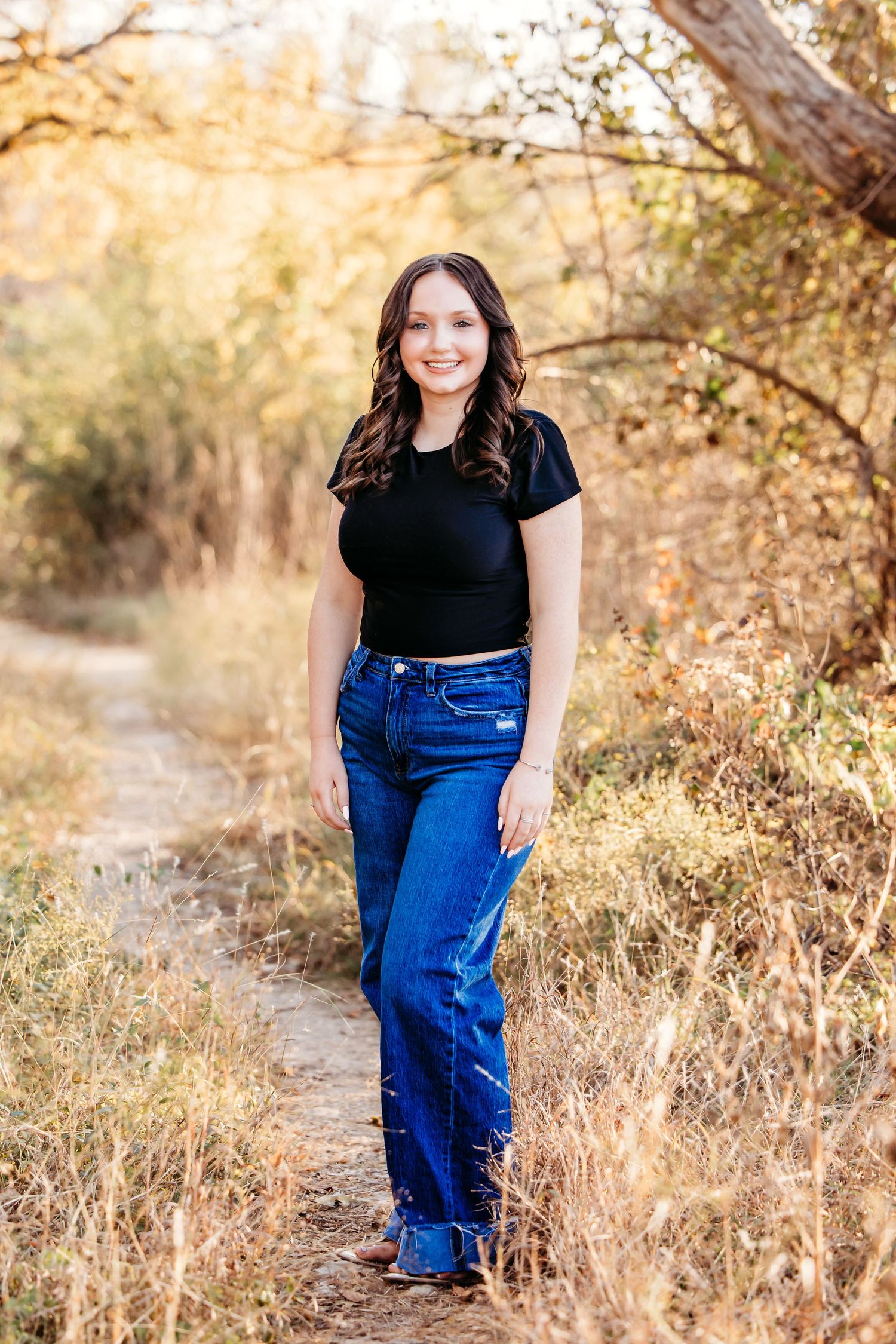 Outdoor portrait photographs featuring senior girl in a black top and blue jeans against an autumn nature backdrop in Fort Worth, TX