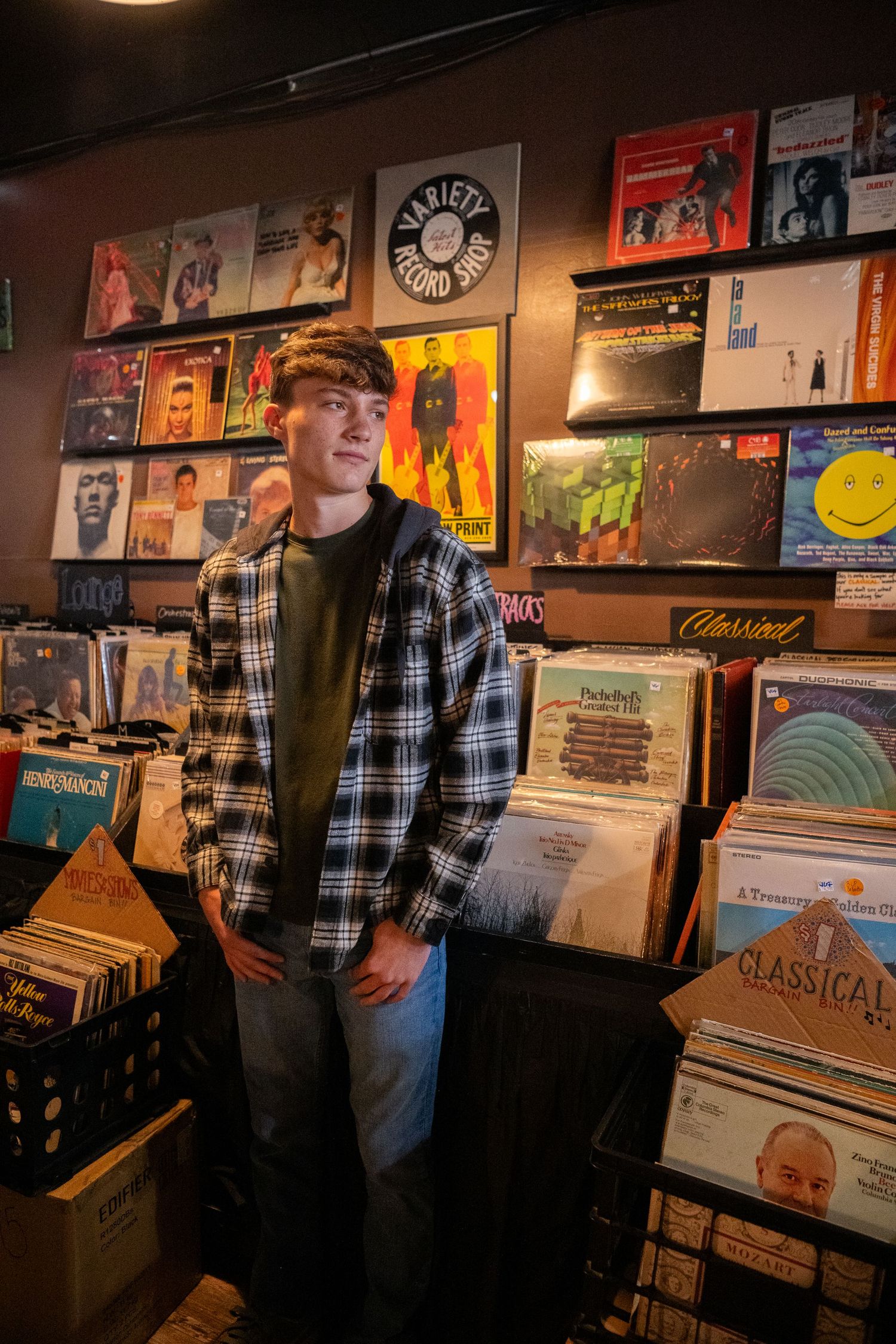 A person browses through vinyl records in a dimly lit record store with album covers displayed on the walls.