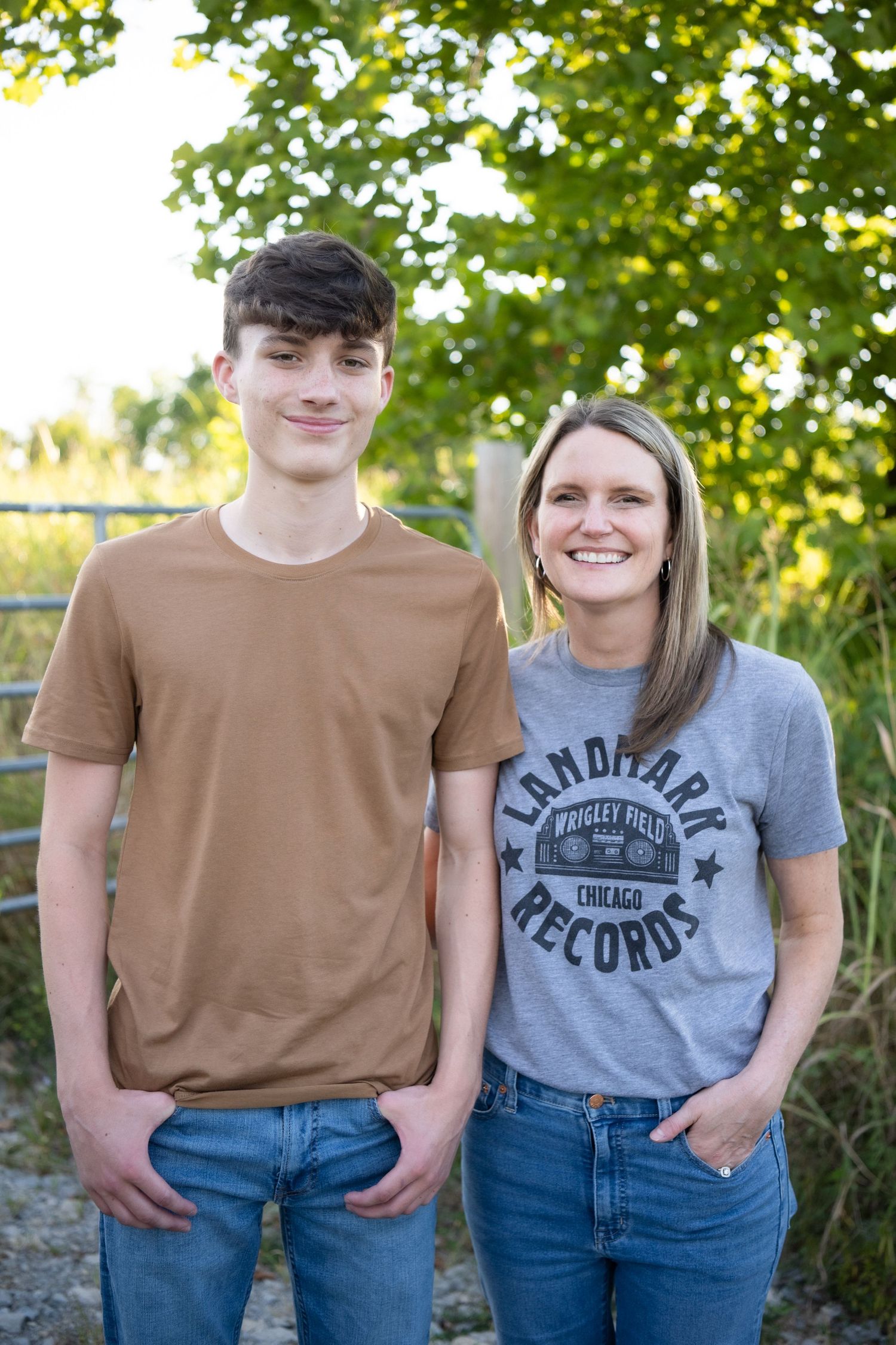 A couple wearing matching brown and gray t-shirts with blue jeans pose together outdoors in a natural setting.