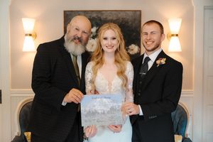 A formal indoor wedding ceremony takes place in an elegant room with wall sconces and white decor.