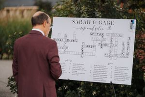 A large decorative wedding check is being signed during a ceremony at an outdoor venue.