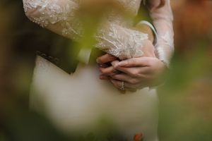 Close-up shot of hands holding a phone while wearing a delicate lace wedding dress in soft natural lighting.