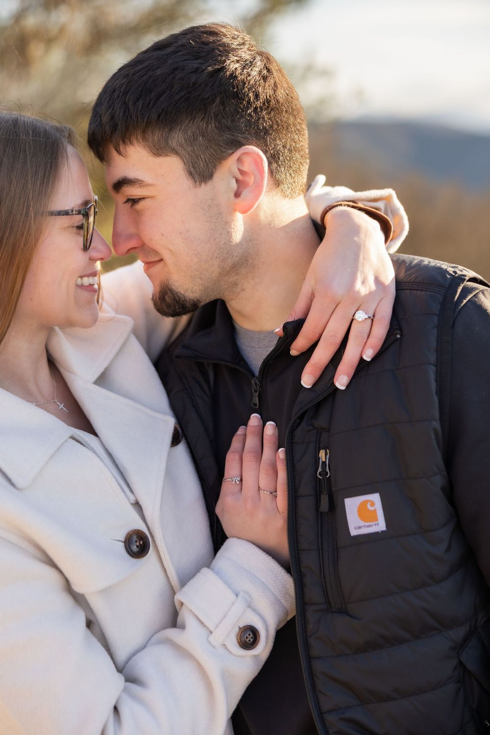 A romantic couple embraces outdoors, with one wearing a white coat and the other in a black Carhartt jacket.