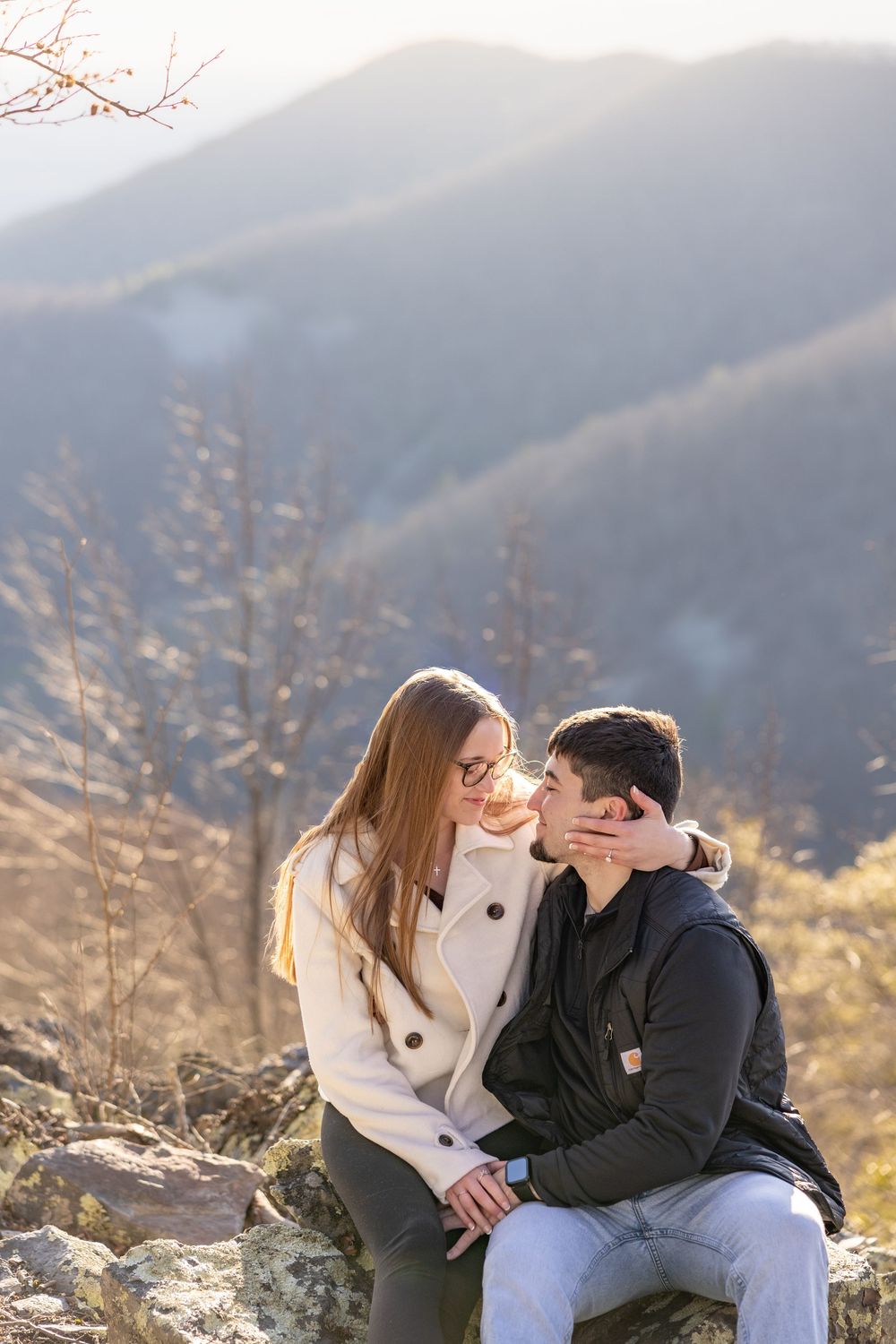 A couple shares tender moments together while sitting outdoors against a scenic mountain backdrop during golden hour.