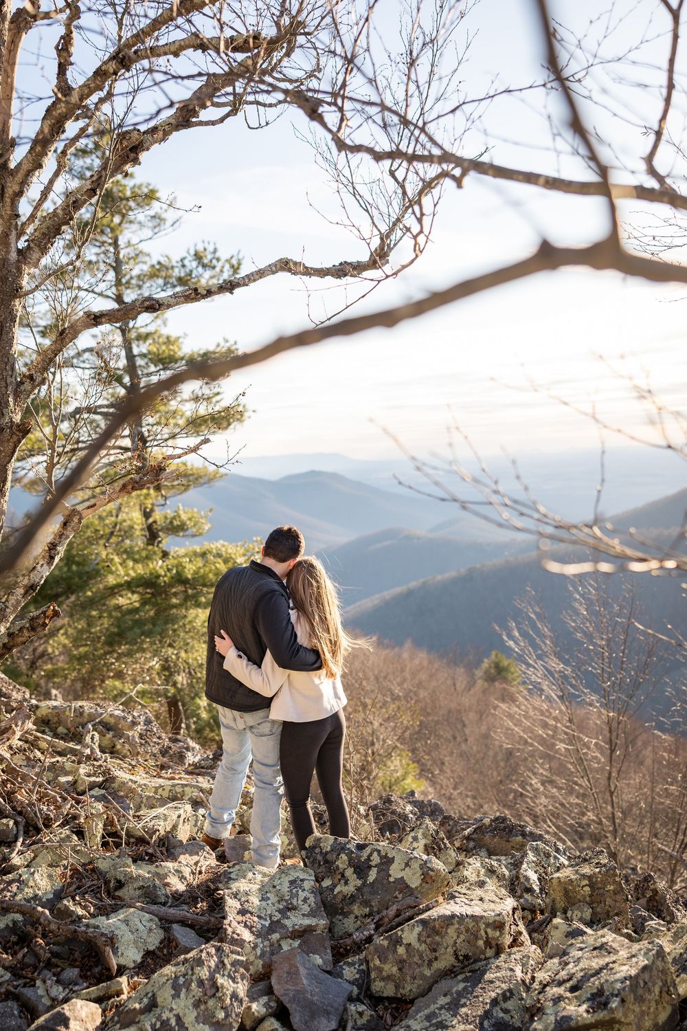 A couple stands together on a rocky mountain overlook enjoying scenic mountain views on a winter afternoon.
