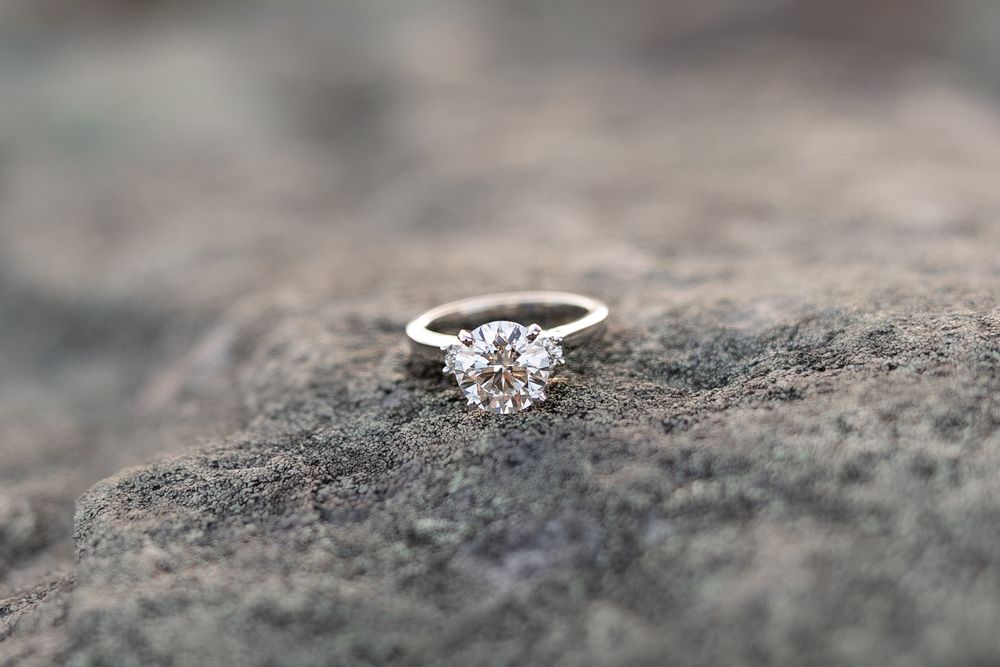 Close up macro shot of a diamond engagement ring resting on a textured stone surface.