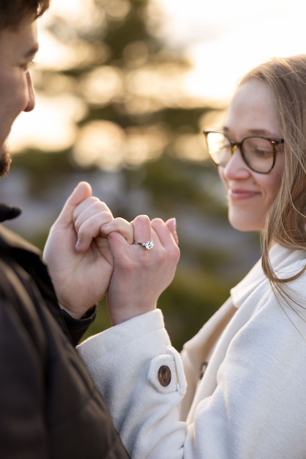 Close up shot of a couple's hands with an engagement ring during a sunset proposal moment.