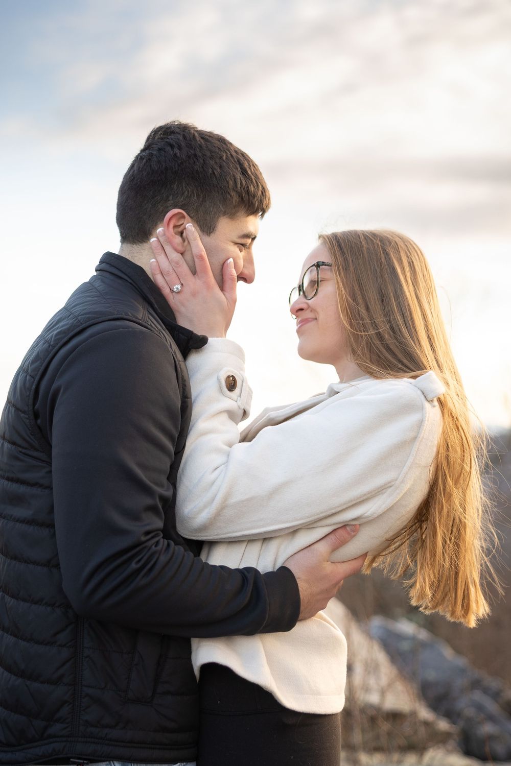 Romantic couple embracing outdoors during golden hour with soft lighting and cloudy sky.